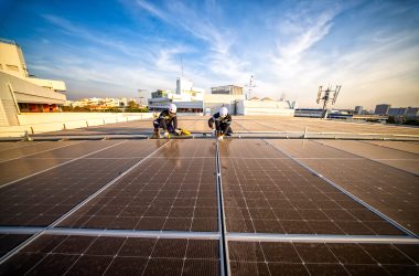 Workers install solar panels on a rooftop in a city during sunset hours Technicians are securing solar panels on a building rooftop in an urban environment as the sun sets, highlighting clean energy efforts and teamwork.